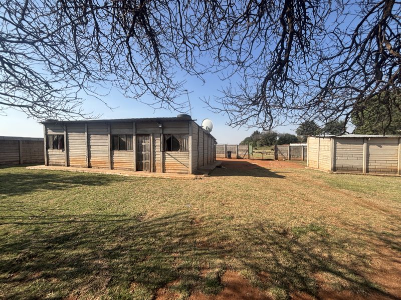 Rear view of a small holding property featuring a precast concrete structure, corrugated metal roofing, and surrounding perimeter walling on a large plot.