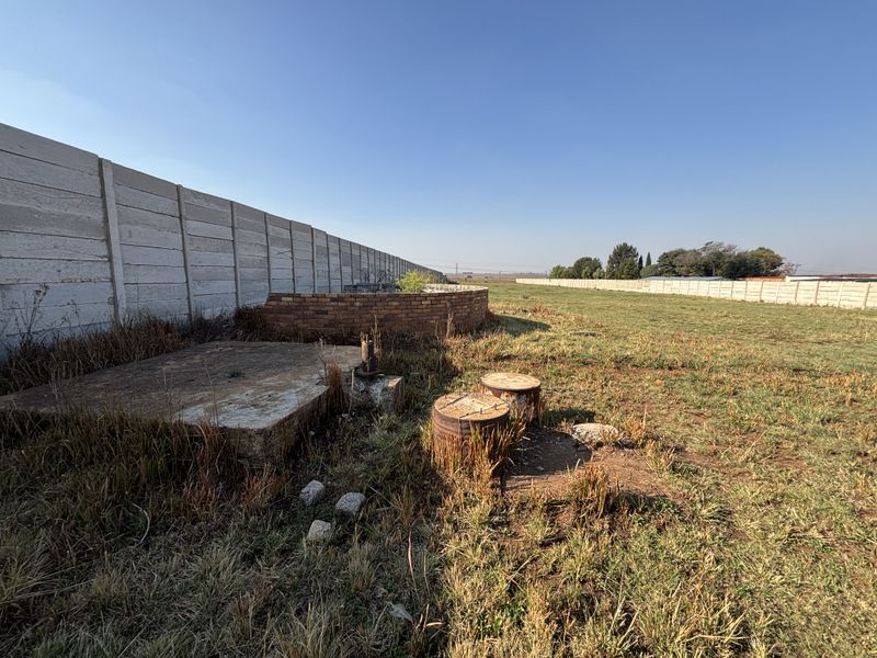 Expansive outdoor area featuring a precast concrete boundary wall, brick retaining wall, and existing borehole infrastructure on a large plot.