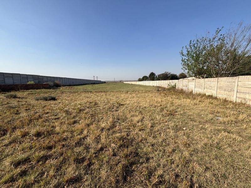 A large, undeveloped plot of land enclosed by precast concrete boundary walls, featuring dry grass and open space.