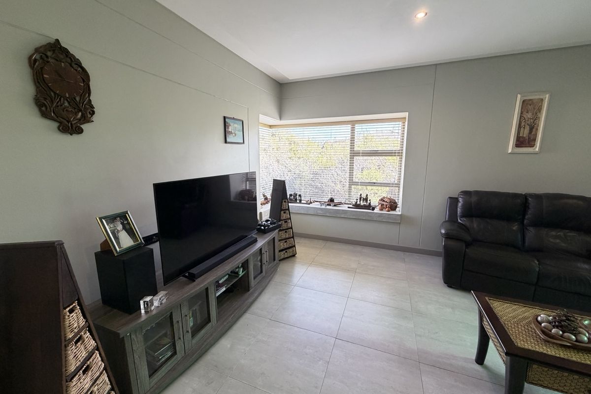 A well-maintained living room featuring neutral tiled flooring, recessed lighting, and a large window with horizontal blinds providing natural light.