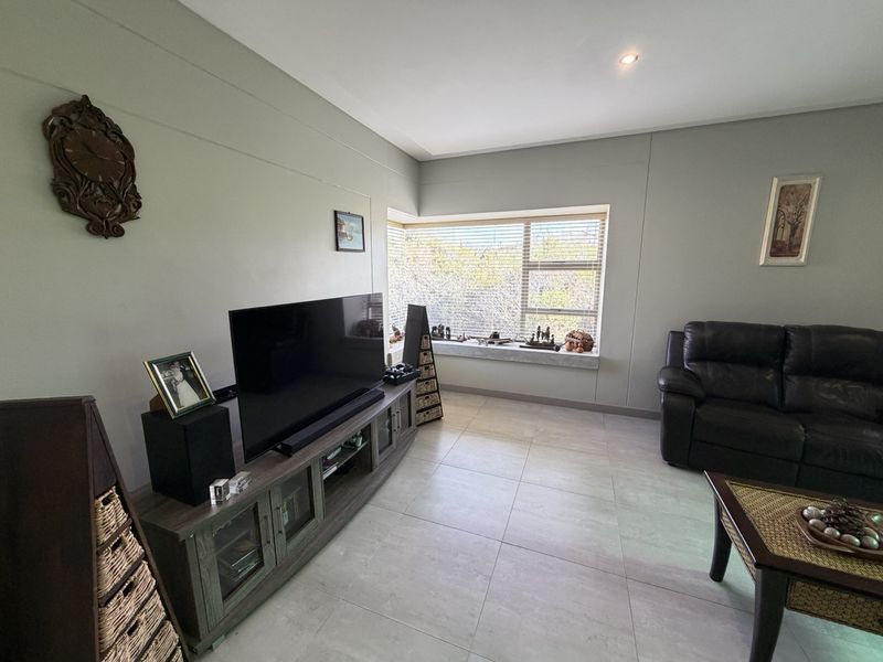 A well-maintained living room featuring neutral tiled flooring, recessed lighting, and a large window with horizontal blinds providing natural light.
