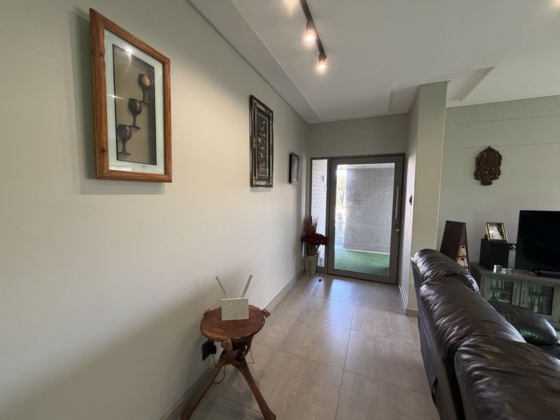 A bright and welcoming entrance hall featuring modern tiled flooring, track lighting, and a glass-paneled front door leading to the exterior.