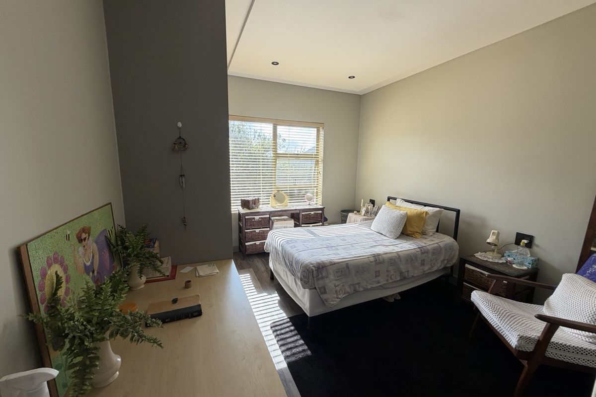 A well-lit bedroom featuring neutral wall tones, laminate flooring, recessed downlighting, and a window fitted with venetian blinds.