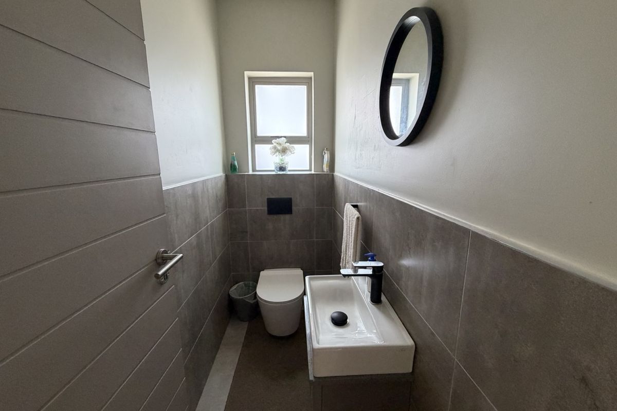 A modern, compact guest bathroom featuring a wall-mounted toilet, vanity basin with a sleek mixer tap, and neutral wall tiling.