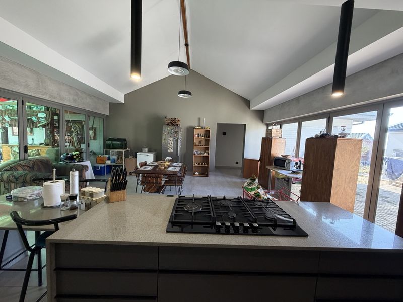 Spacious open-plan living and kitchen area featuring a vaulted ceiling, modern gas hob, stone island countertop, and large sliding doors leading to the exterior.