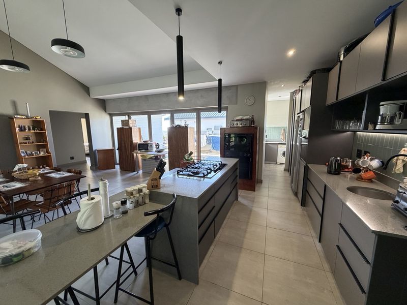 Spacious open-plan kitchen and dining area featuring a central island with gas hob, modern cabinetry, stone countertops, and large sliding doors leading outdoors.