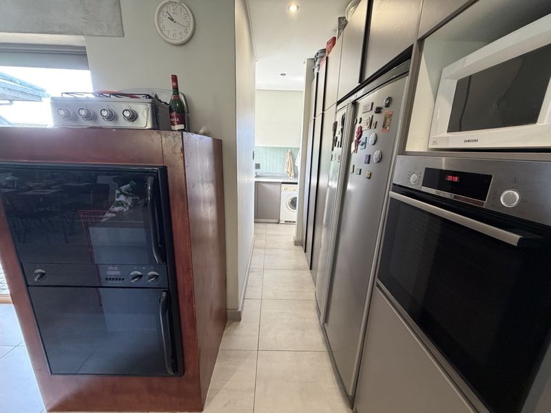 A functional kitchen area featuring built-in oven and microwave units, ample cabinetry, and tiled flooring, leading through to a laundry space.