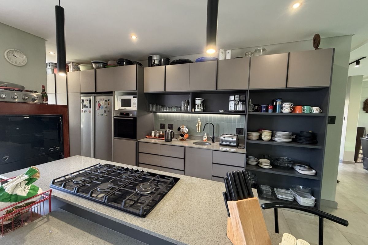 Modern kitchen featuring dark grey cabinetry, stone countertops, a central island with a gas cooktop, and integrated appliances.