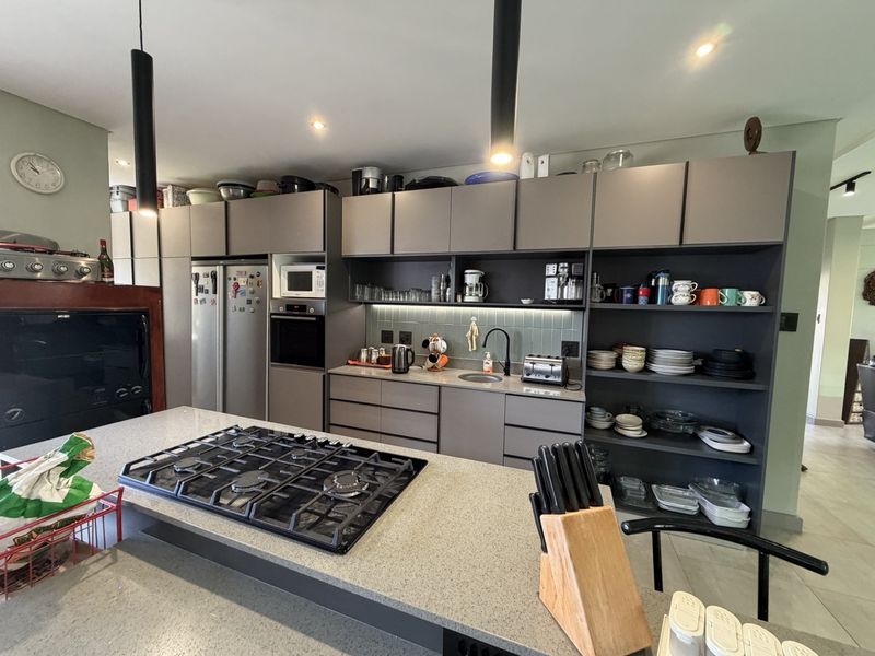 Modern kitchen featuring dark grey cabinetry, stone countertops, a central island with a gas cooktop, and integrated appliances.