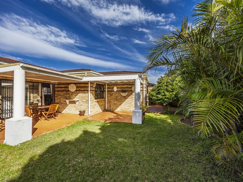 A well-maintained rear exterior featuring a covered tiled patio, brick facade, and a private garden area with established landscaping.