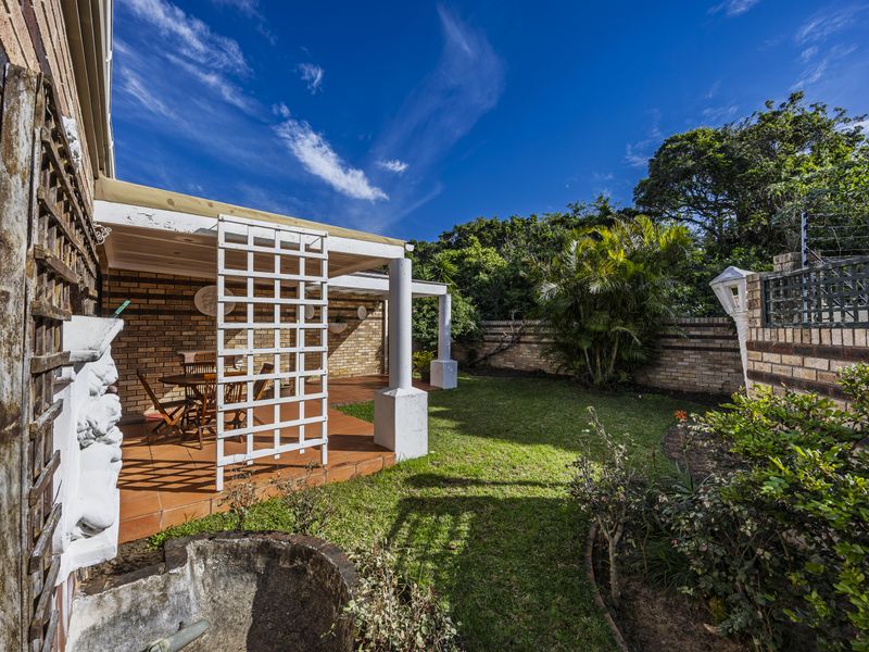 A private rear garden featuring a covered patio with tiled flooring, brick walls, and established landscaping, offering a peaceful outdoor living space.