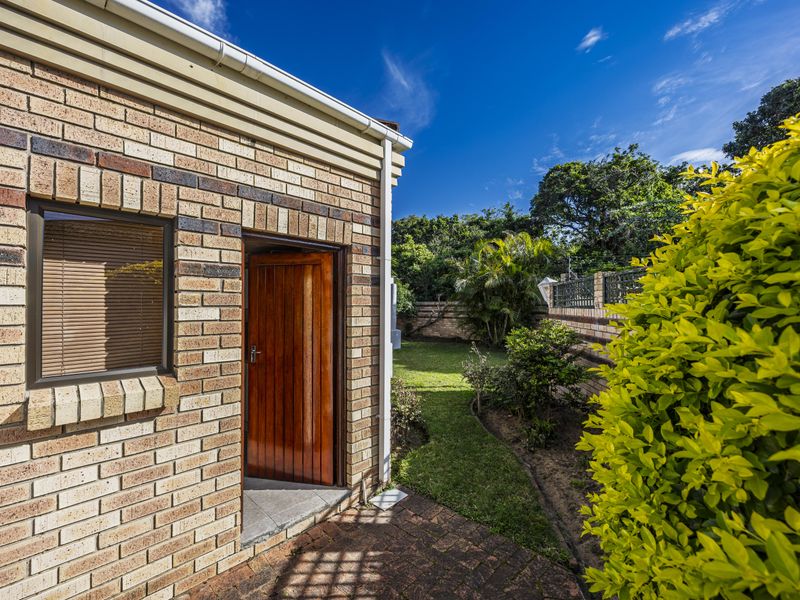 A view of the rear exterior featuring a face brick facade, a timber door leading to the interior, and a well-maintained garden with paved patio.