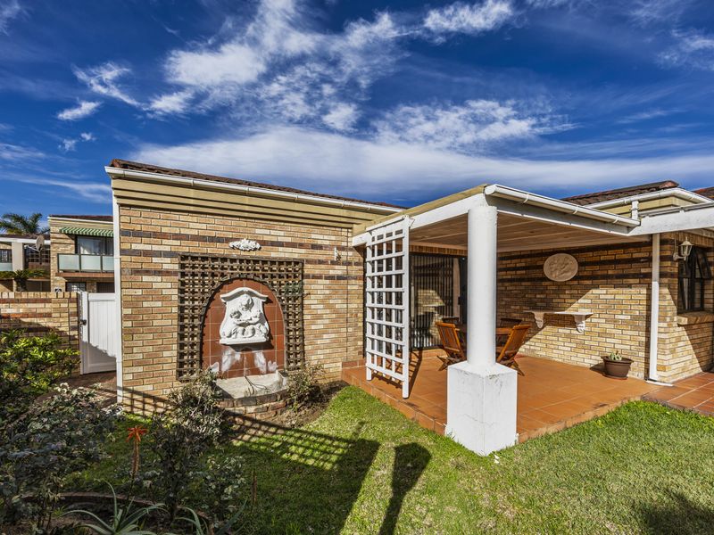 A covered brick-paved patio area featuring a decorative wall-mounted water feature, integrated support columns, and direct access to the interior via sliding glass doors.