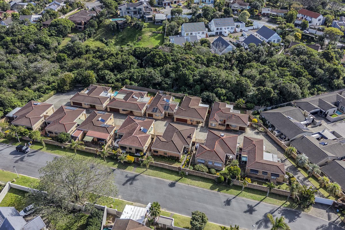 Aerial view of a townhouse complex featuring multiple residential units with tiled roofs, paved driveways, and established surrounding greenery.