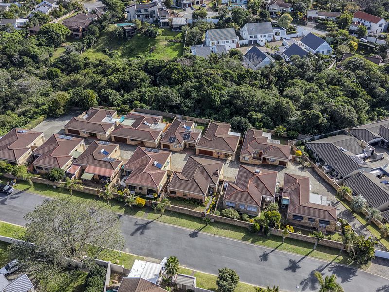 Aerial view of a townhouse complex featuring multiple residential units with tiled roofs, paved driveways, and established surrounding greenery.