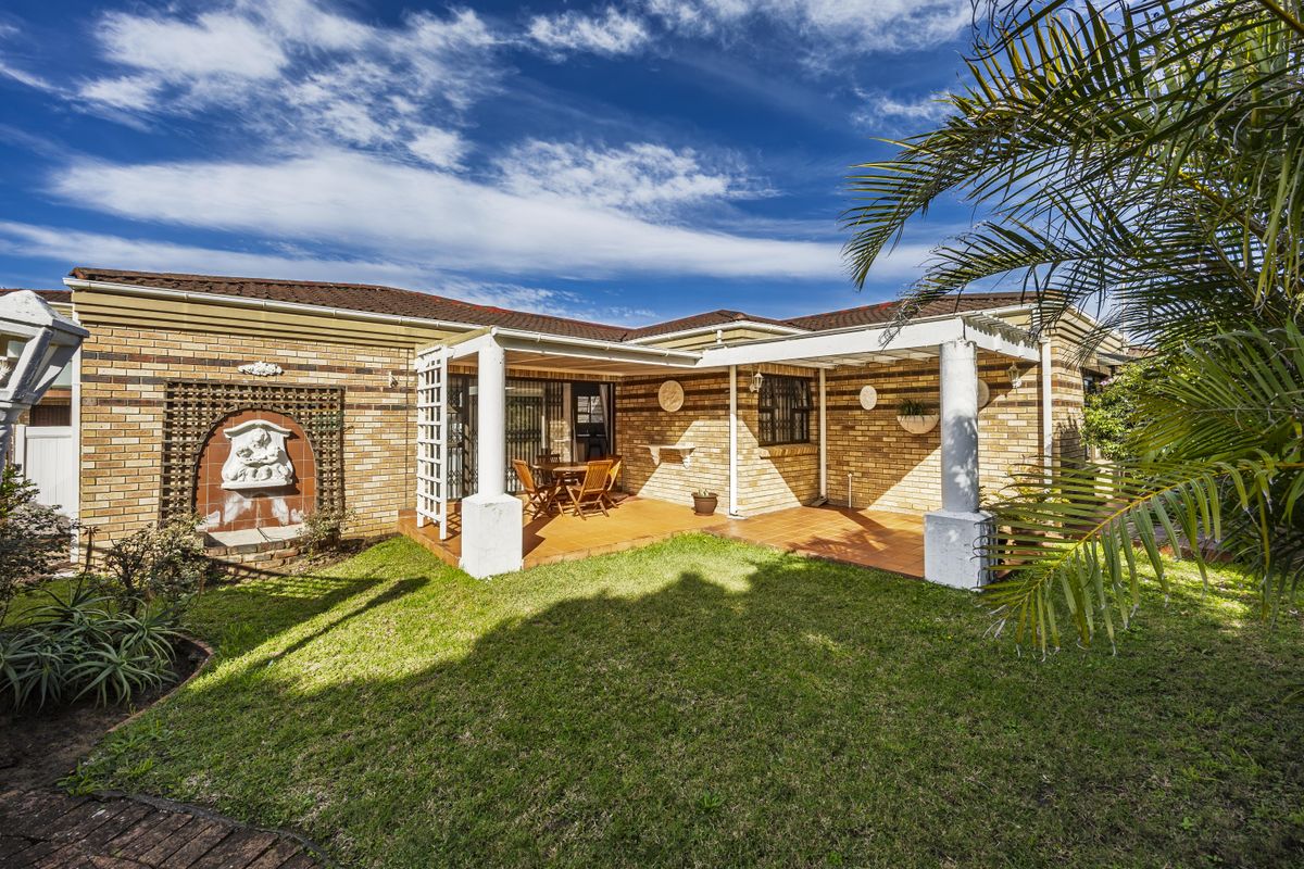 A well-maintained rear exterior featuring a covered brick patio, pergola, and a landscaped garden with a decorative wall fountain.