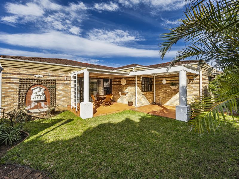 A well-maintained rear exterior featuring a covered brick patio, pergola, and a landscaped garden with a decorative wall fountain.