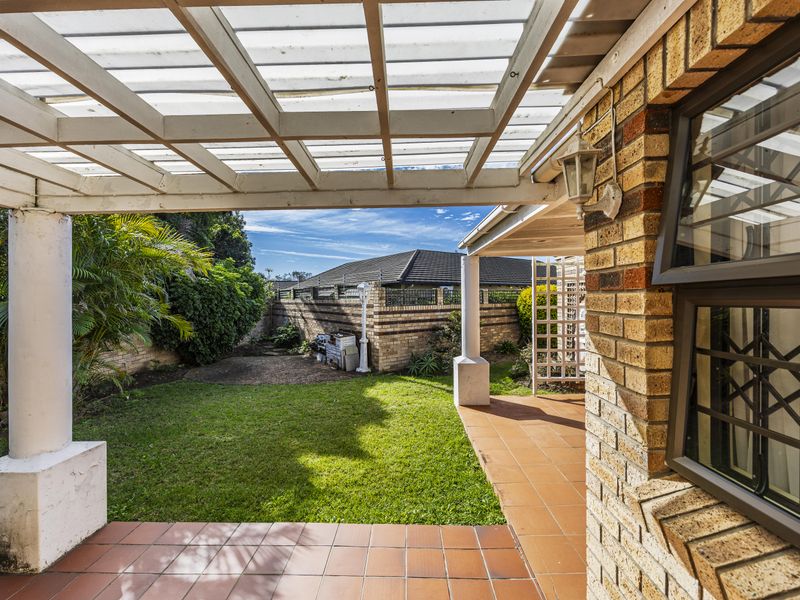 A covered patio area featuring a pergola, tiled flooring, and direct access to a private garden space with brick boundary walls.