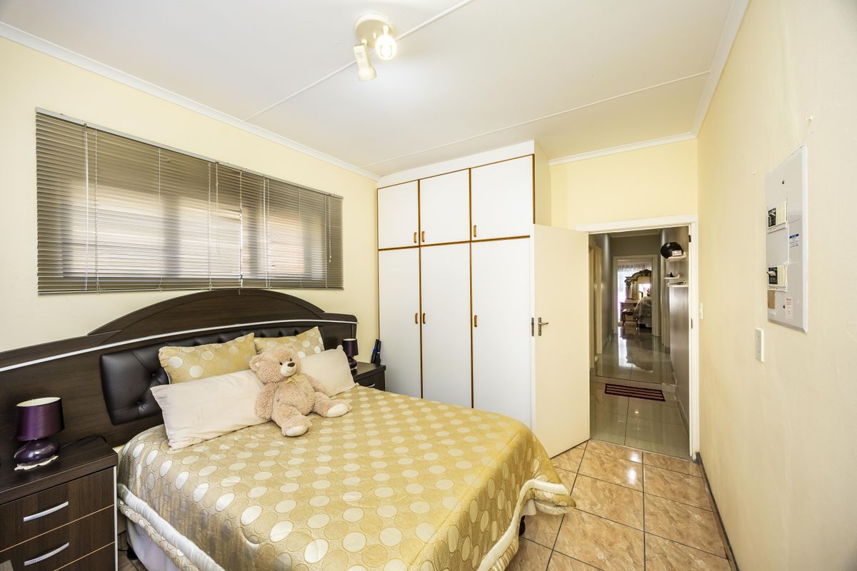 A functional bedroom featuring built-in cupboards, tiled flooring, and venetian blinds, offering a practical layout with direct access to the hallway.