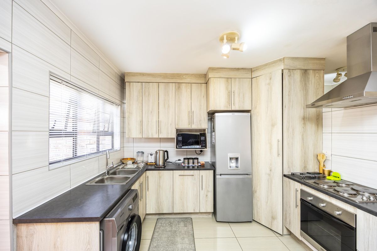Modern kitchen featuring light wood-grain cabinetry, dark laminate countertops, stainless steel appliances, and tiled finishes throughout.