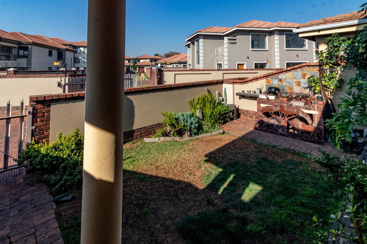 A private rear garden featuring a paved patio area, a built-in braai with stone cladding, and a brick boundary wall within a cluster complex.