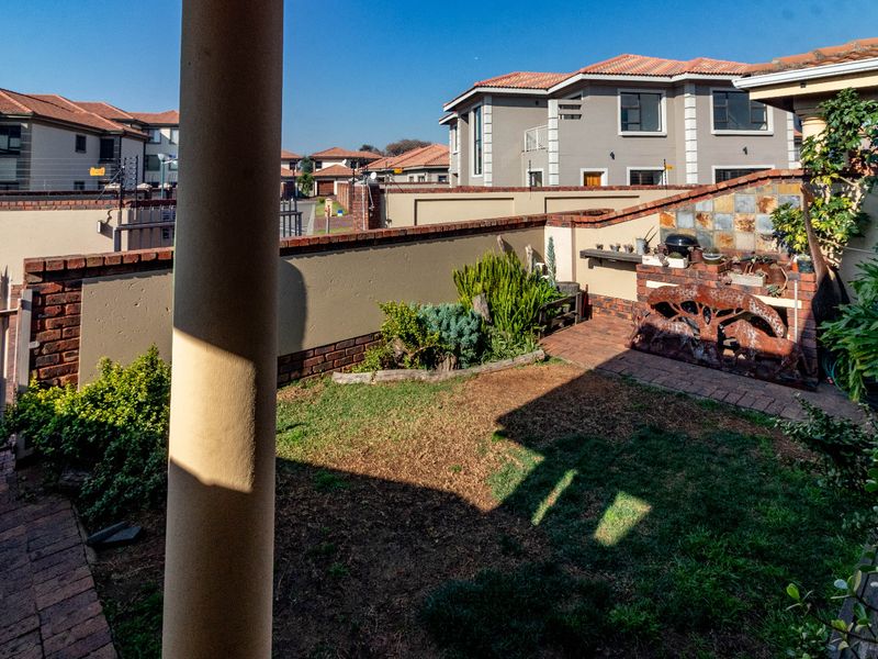 A private rear garden featuring a paved patio area, a built-in braai with stone cladding, and a brick boundary wall within a cluster complex.