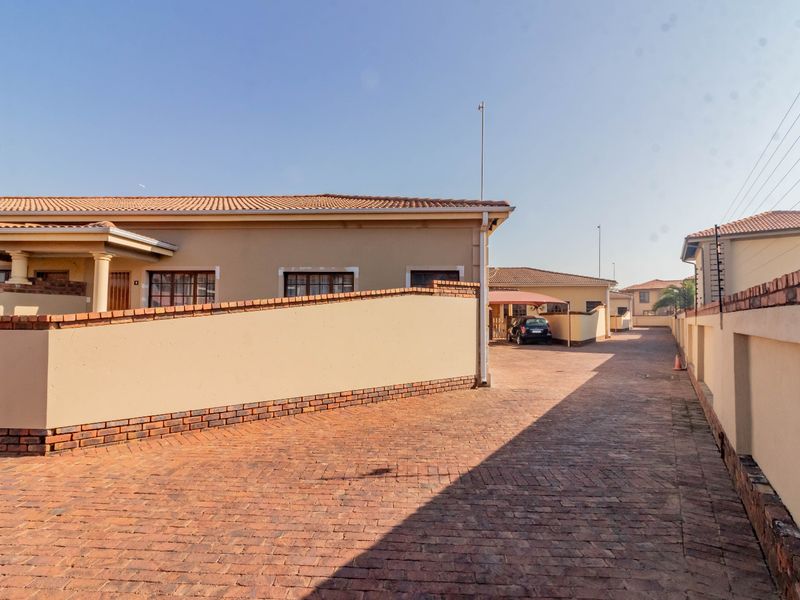 A view of the paved driveway and exterior facade of the cluster home, featuring perimeter walling and a carport.