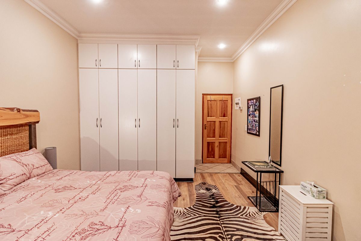 A well-maintained bedroom featuring extensive built-in white cupboards, recessed downlighting, and warm laminate flooring, providing ample storage and a clean aesthetic.