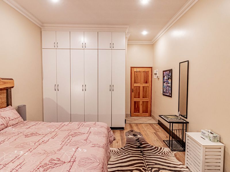 A well-maintained bedroom featuring extensive built-in white cupboards, recessed downlighting, and warm laminate flooring, providing ample storage and a clean aesthetic.
