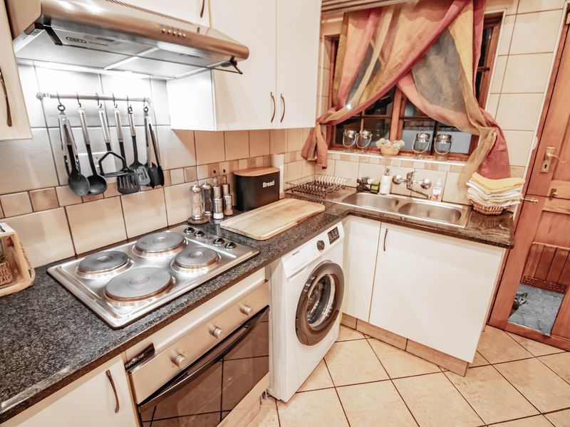 Compact kitchen featuring granite countertops, built-in oven, electric hob, extractor fan, double sink, and integrated washing machine with tiled finishes.