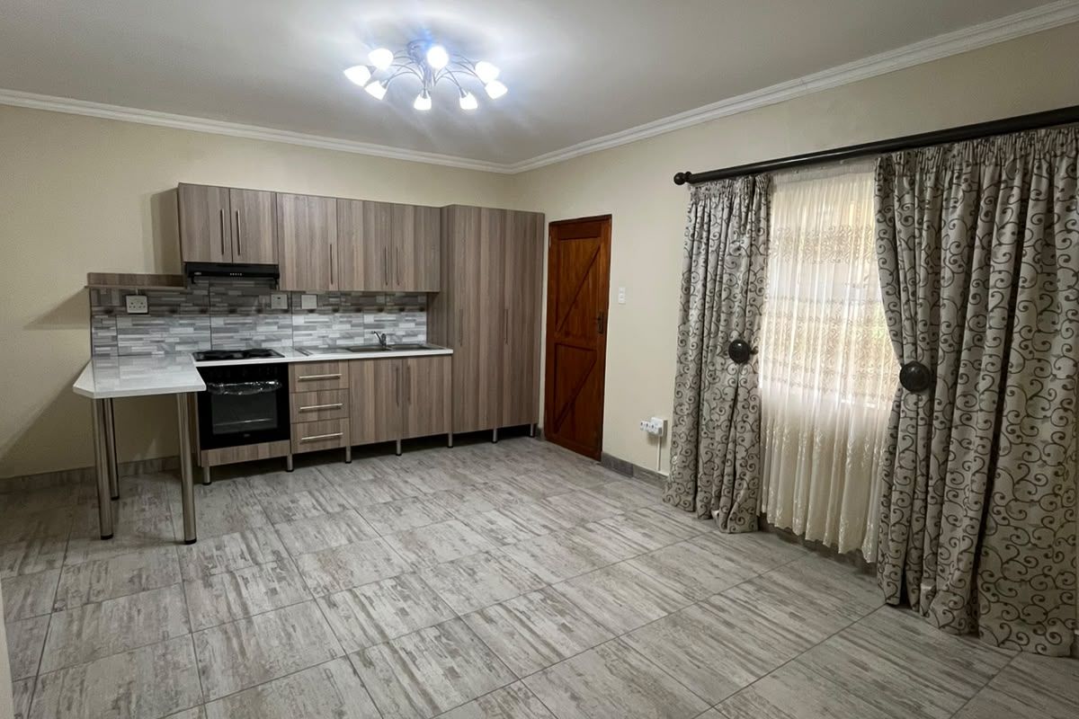 An open-plan living and kitchen area featuring modern wood-finish cabinetry, built-in appliances, tiled flooring, and neutral wall tones.