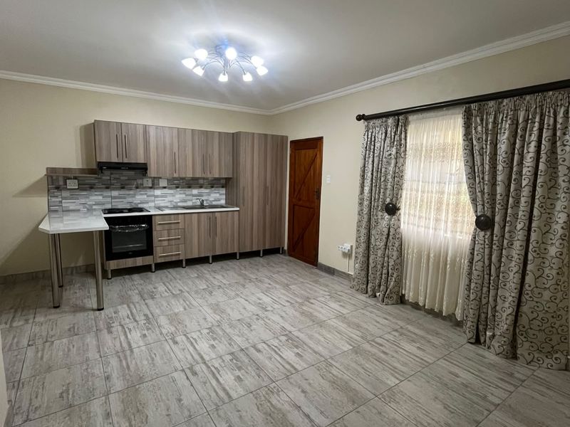 An open-plan living and kitchen area featuring modern wood-finish cabinetry, built-in appliances, tiled flooring, and neutral wall tones.