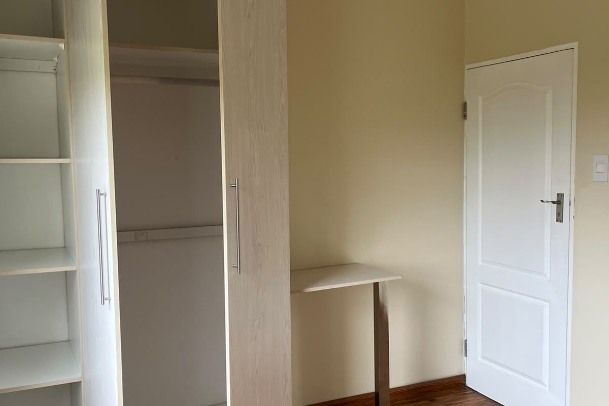 A bright bedroom featuring light wood-grain built-in wardrobes, a matching integrated desk, and warm-toned laminate flooring.
