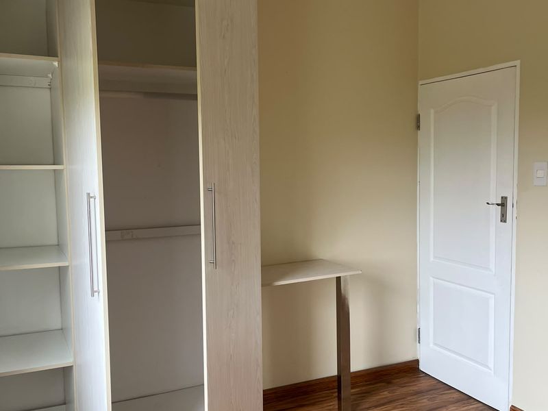 A bright bedroom featuring light wood-grain built-in wardrobes, a matching integrated desk, and warm-toned laminate flooring.