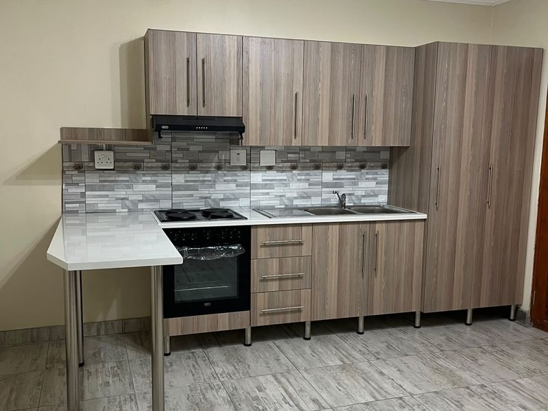 Modern kitchen featuring wood-look cabinetry, integrated electric oven and hob, tiled backsplash, and durable tiled flooring in a clean, well-maintained space.