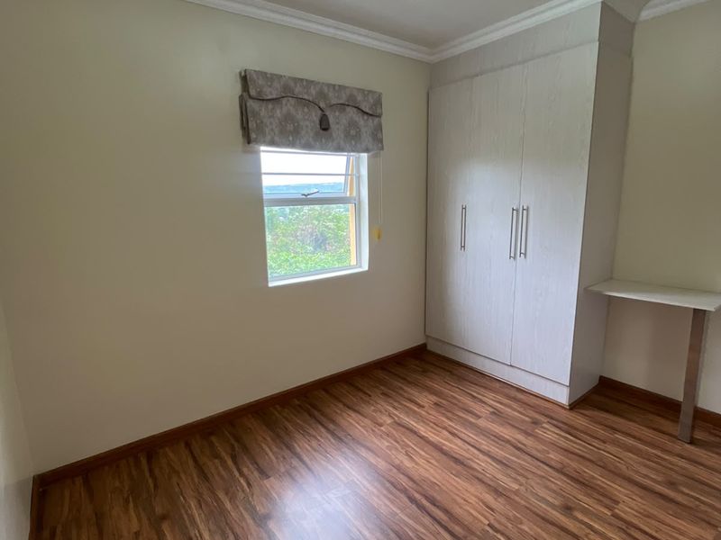 A bright, empty bedroom featuring laminate flooring, a built-in wardrobe, and a built-in desk, offering a clean and functional space.