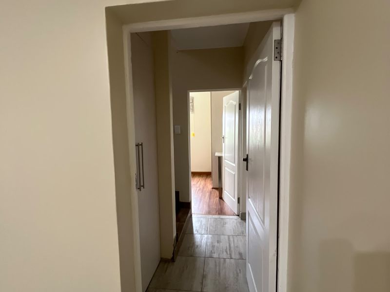 A clean, neutral hallway featuring tiled flooring and built-in storage, providing access to adjacent rooms within the flat.