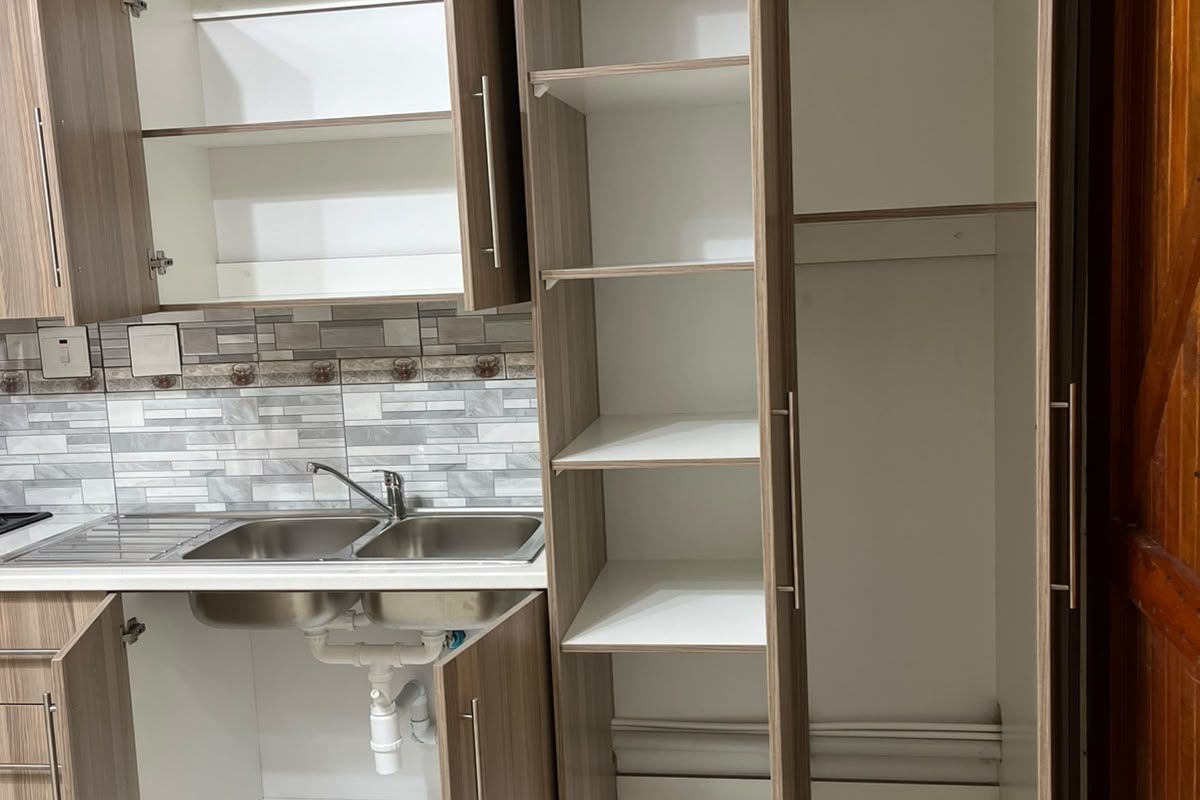 A functional kitchen area featuring built-in cabinetry, a double bowl stainless steel sink with mixer tap, and decorative tiled backsplash.