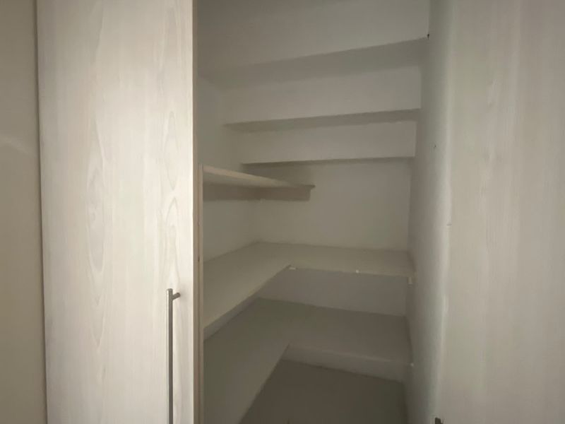 A clean, empty walk-in pantry or scullery featuring built-in white shelving and light wood-grain cabinetry doors.