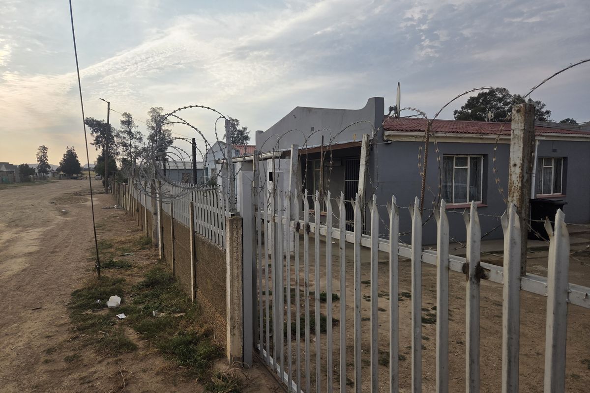 Front exterior view of a residential property featuring a metal palisade fence with razor wire security and a tiled roof structure.