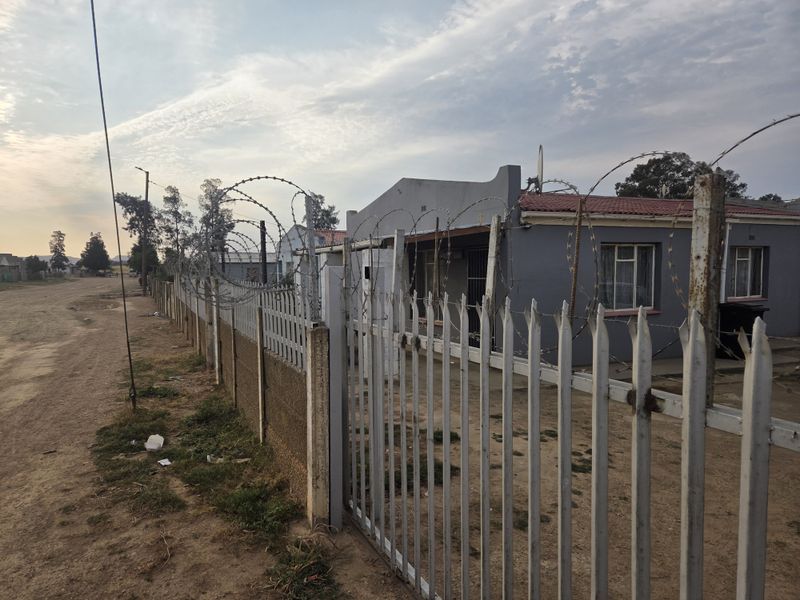 Front exterior view of a residential property featuring a metal palisade fence with razor wire security and a tiled roof structure.