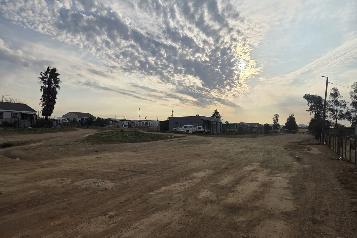 A wide-angle view of a residential street with unpaved road surfaces and surrounding neighborhood properties under a cloudy sky.