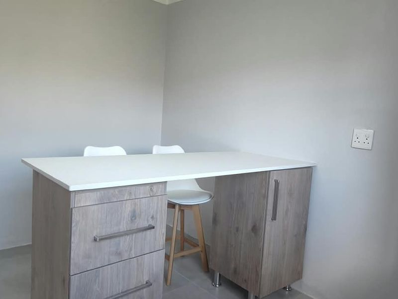 A compact kitchen area featuring a modern wood-finish island with built-in storage and drawers, set against neutral painted walls.