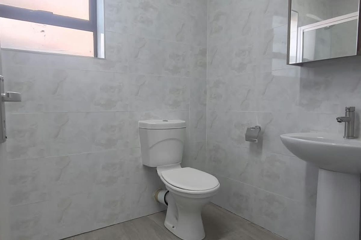 A clean, modern bathroom featuring tiled walls, a pedestal washbasin, and a standard toilet.