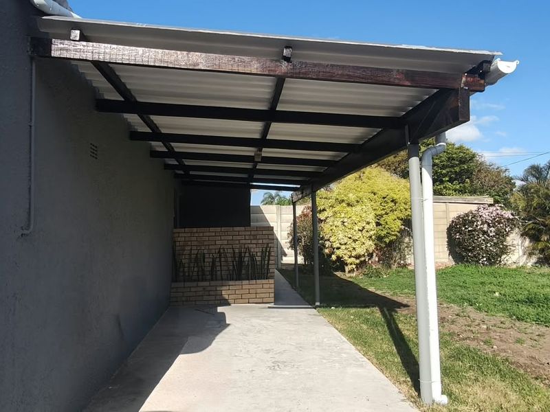 A covered outdoor patio area featuring a corrugated roof, timber beams, and a brick privacy wall, overlooking the rear garden space.