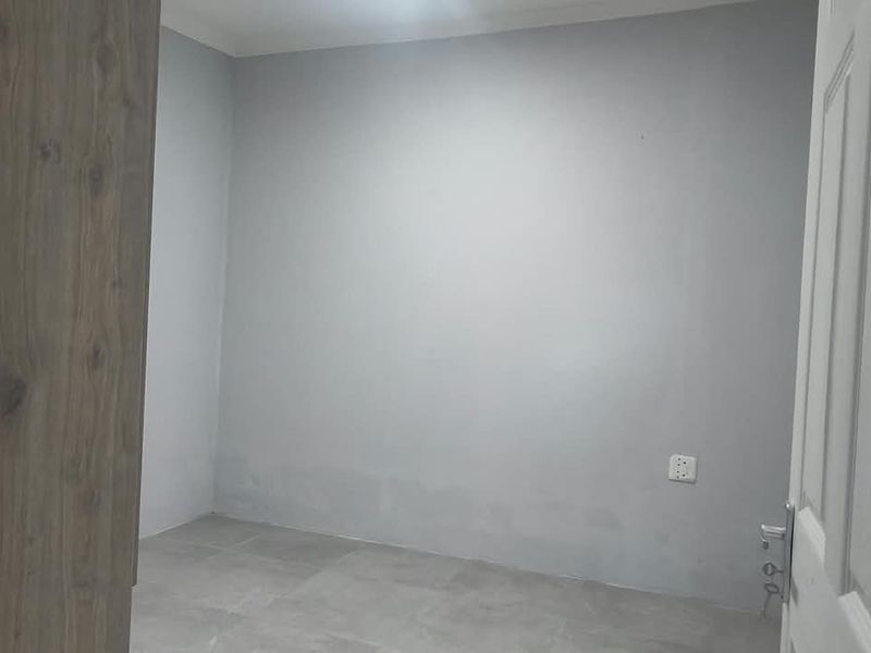 An empty bedroom featuring neutral grey walls, tiled flooring, and a built-in wooden cupboard, offering a blank canvas for personalization.
