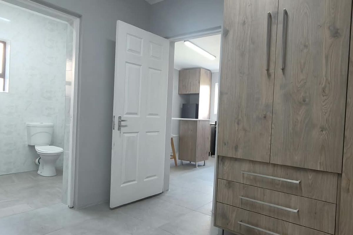 A clean bedroom featuring built-in wooden wardrobes, tiled flooring, and direct access to an en-suite bathroom and adjacent living area.