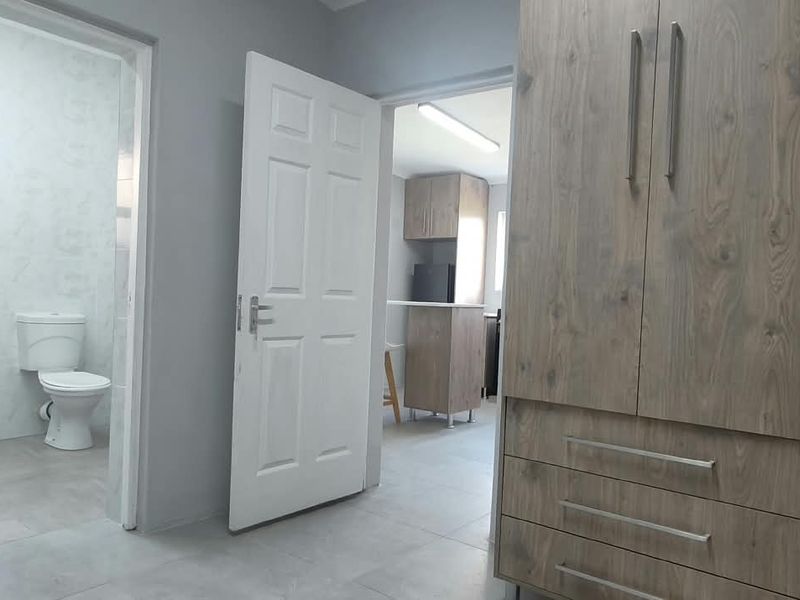 A clean bedroom featuring built-in wooden wardrobes, tiled flooring, and direct access to an en-suite bathroom and adjacent living area.