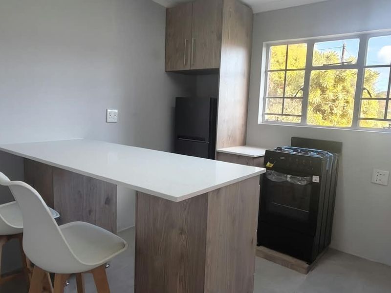 Modern kitchen featuring wood-finish cabinetry, a breakfast bar with stone countertop, and a functional layout with a window providing natural light.