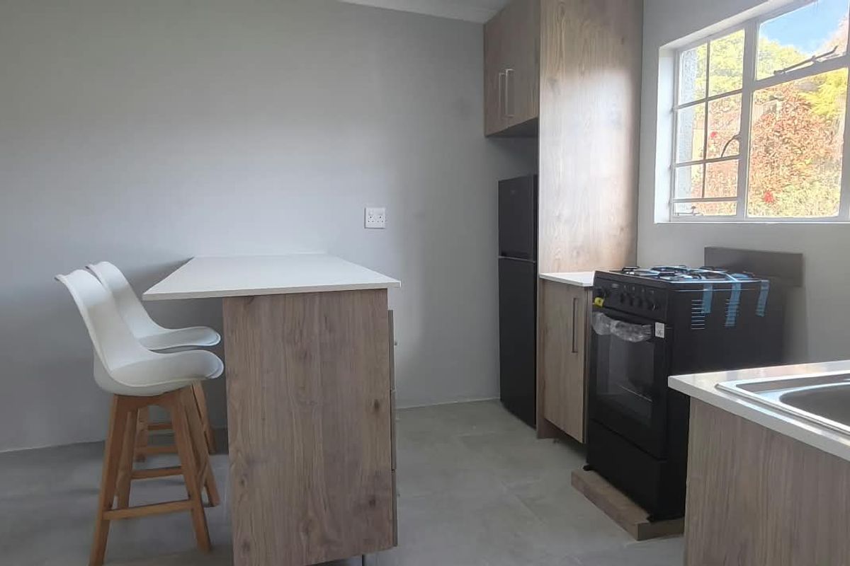 A modern, compact kitchen featuring wood-finish cabinetry, a gas stove with oven, stainless steel sink, and a breakfast bar area with tiled flooring.